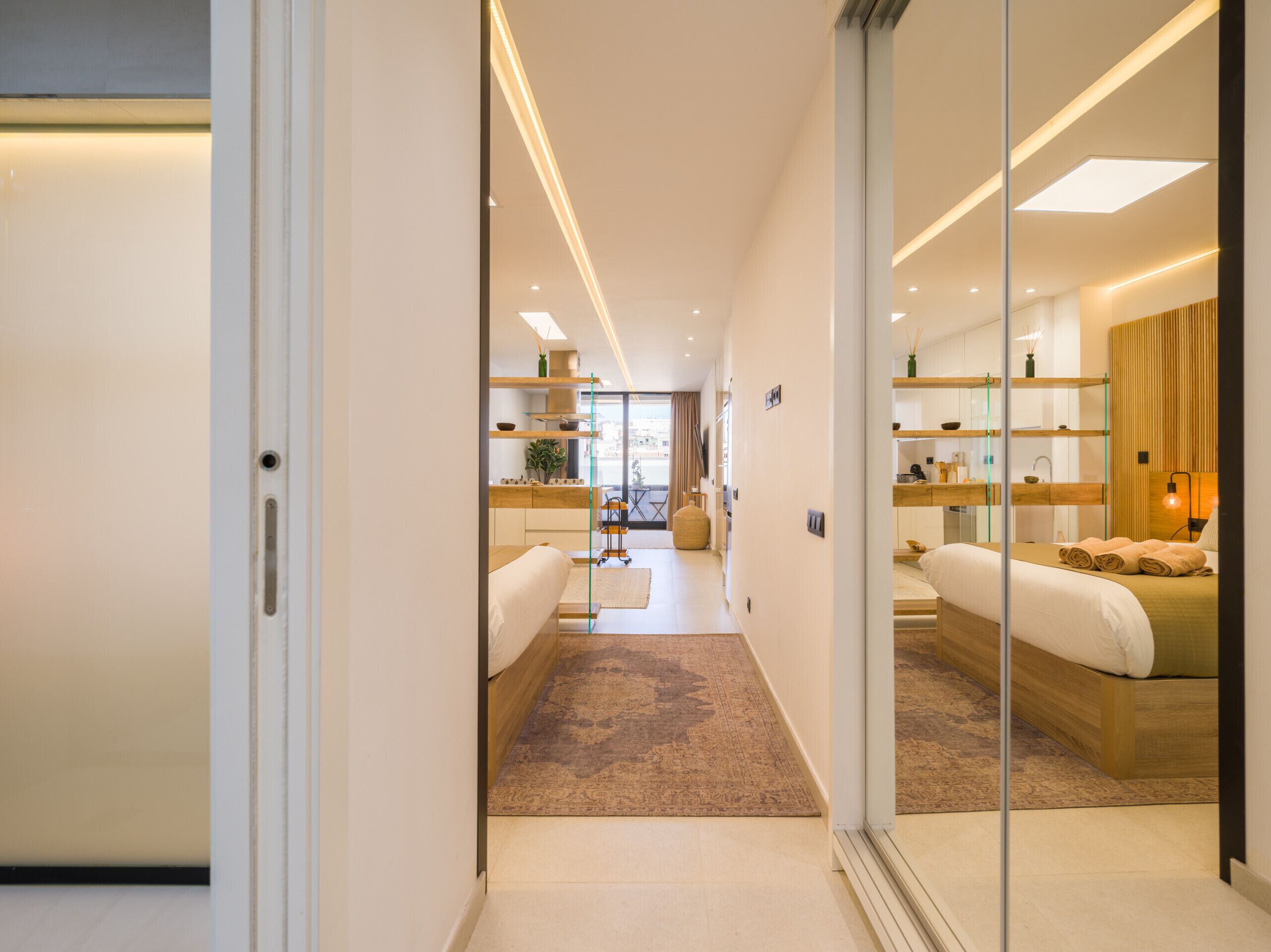 Una habitación de hotel moderna con una cama grande, una zona de estar, una kitchenette y un separador de vidrio.