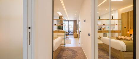 Una habitación de hotel moderna con una cama grande, una zona de estar, una kitchenette y un separador de vidrio.