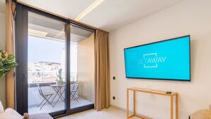 A modern living room with a large TV displaying "GETAWAY", a sliding glass door leading to a balcony, and a minimalist wooden console table.