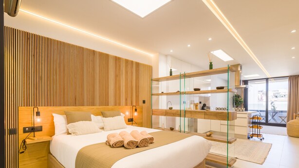 A modern bedroom with a wooden headboard, a glass shelf unit, and a view of the city.