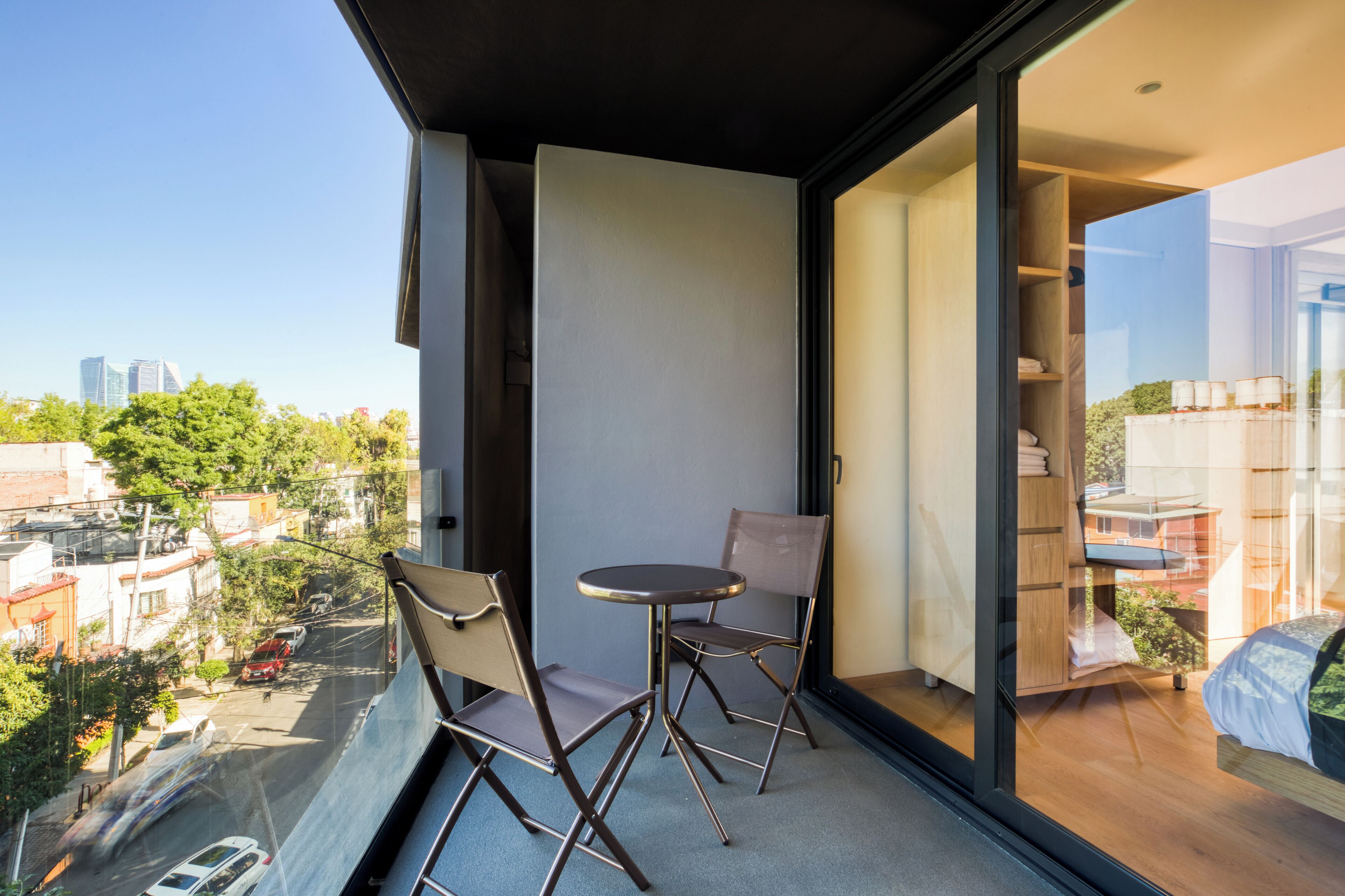 A balcony with a table and chairs, a view of the city, and a glimpse of the interior.