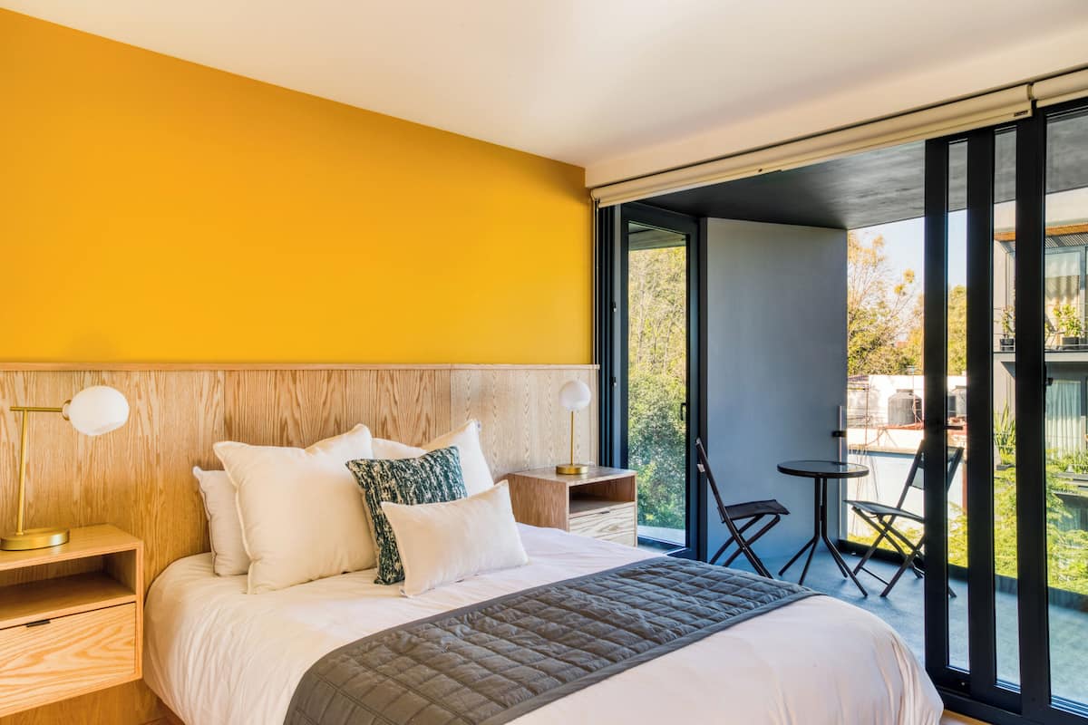 Ein modernes Schlafzimmer mit einem großen Bett, einem Holz-Kopfteil und Blick ins Freie durch große Schiebetüren.