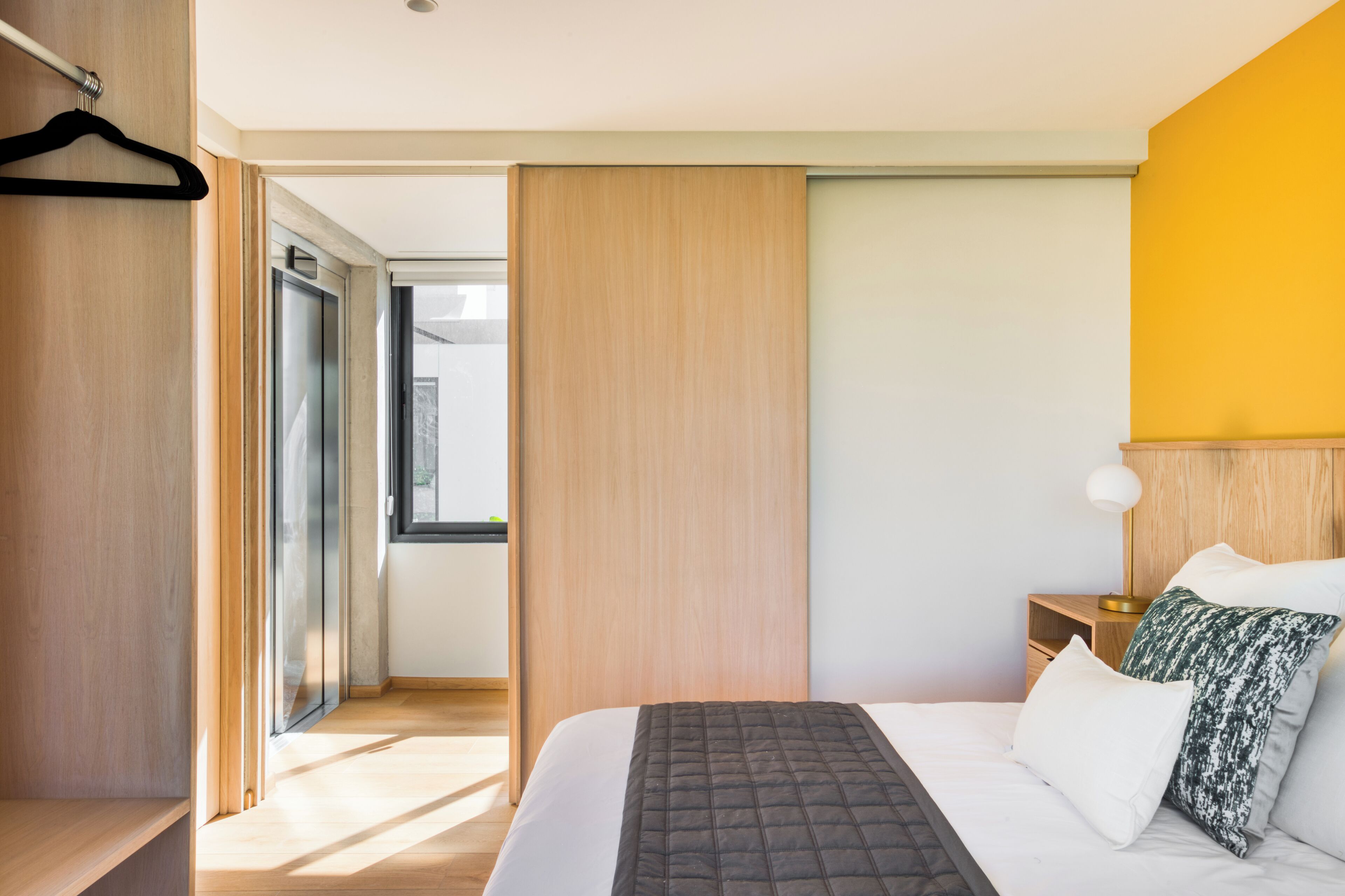 A modern hotel room with a bed, bedside table, and a view through a glass door.