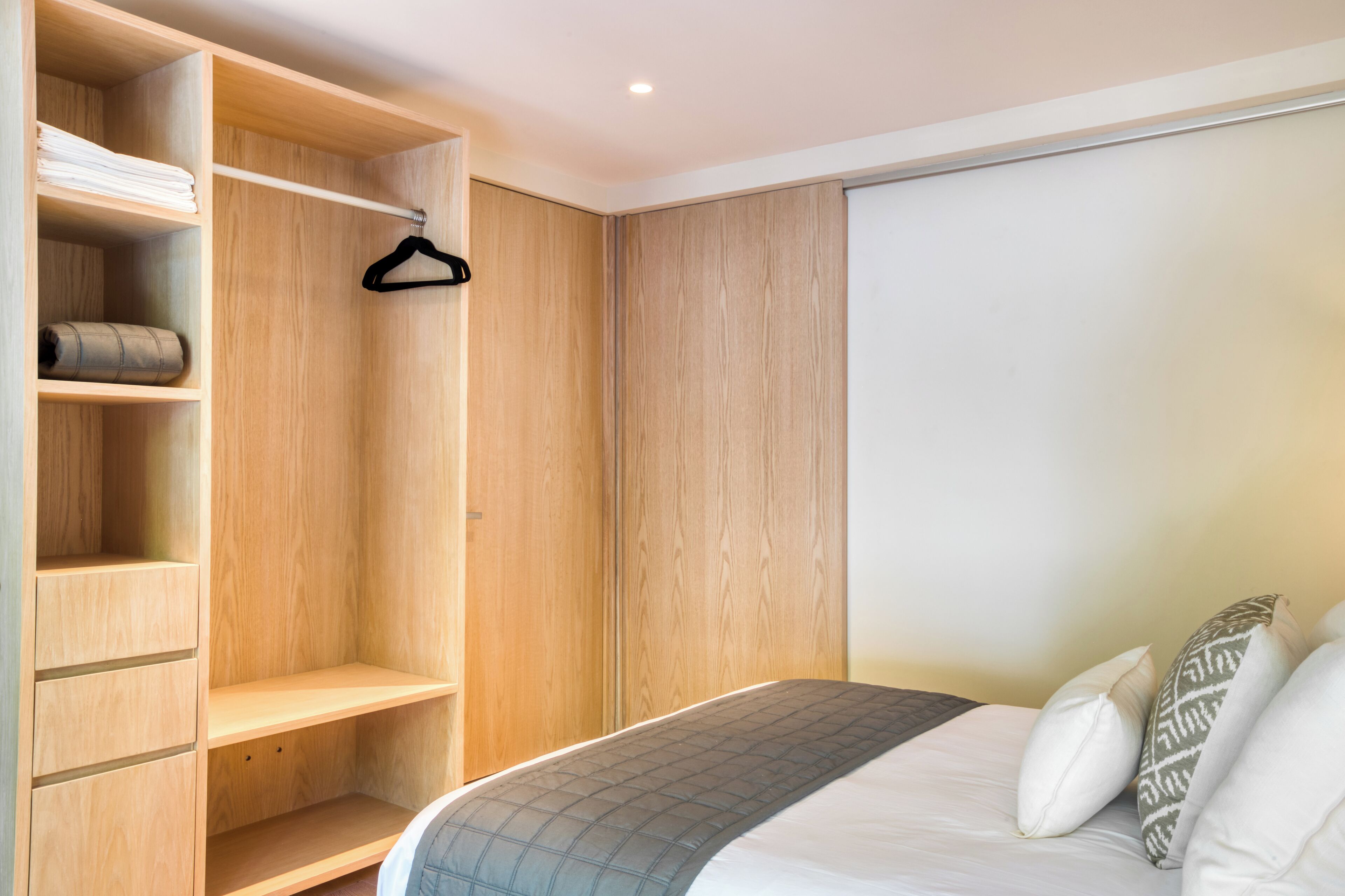 Une chambre à coucher avec une armoire en bois, un lit recouvert d’une couvre-lit à motifs et un vêtement suspendu à l’armoire.