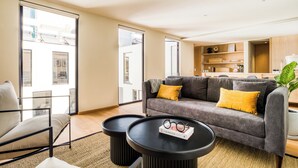 Een moderne woonkamer met een grijze bank, twee zwarte bijzettafeltjes en een groot raam met uitzicht op de stad.