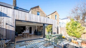 A modern house with a large open patio area, a dining space, and a kitchen visible through a glass door.