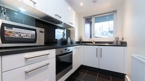 A modern kitchen with white cabinets, a black countertop, and a Panasonic microwave. - Modern 2 bedroom and 2 Bath Apartment in London - Pass the Keys (Edgware)