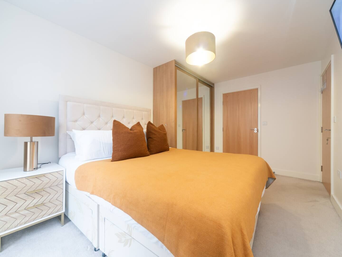 Une chambre à coucher comprenant un lit, une table de chevet, une lampe, un miroir et une armoire.