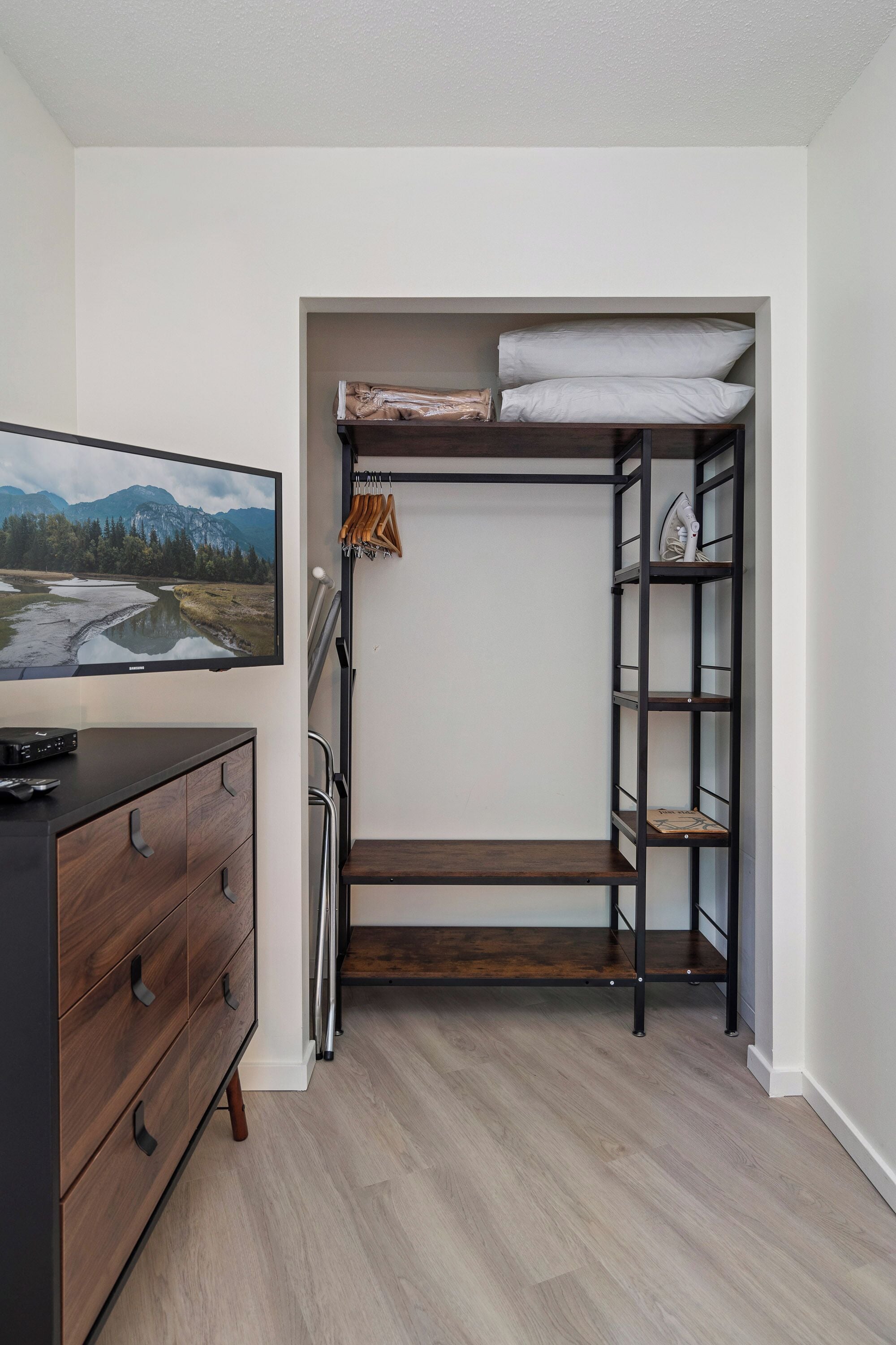 Une petite pièce comprenant un lit superposé, une commode en bois et un téléviseur fixé au mur qui diffuse un paysage.