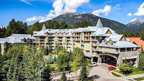 A large hotel with multiple balconies, a central entrance, and a mountainous backdrop. - Ace Cascade (Whistler)