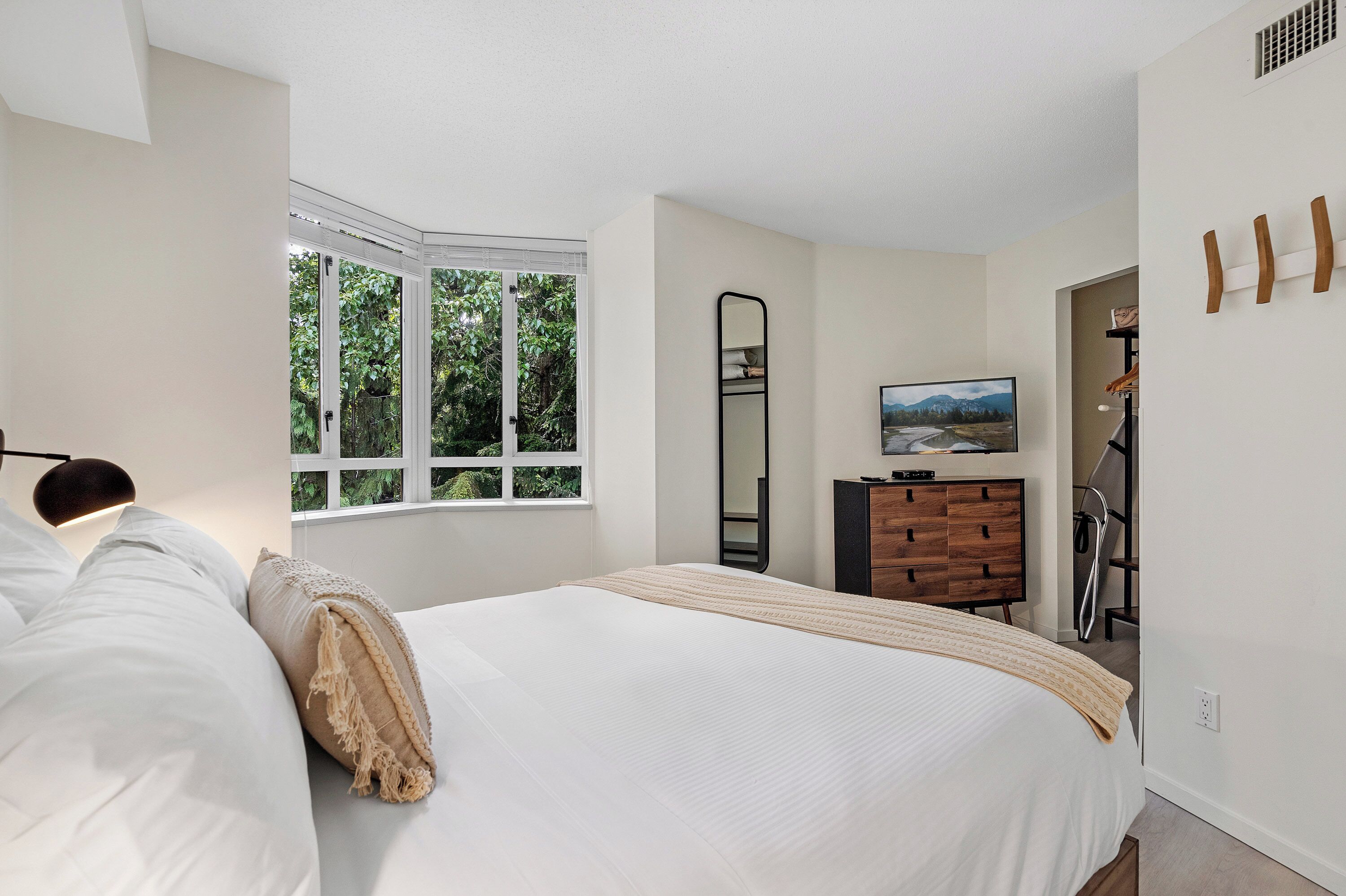 Ein Schlafzimmer mit einem großen Bett, einem Fenster mit Blick auf Grünflächen, einem Schminktisch, einem Spiegel und einem Fernseher.