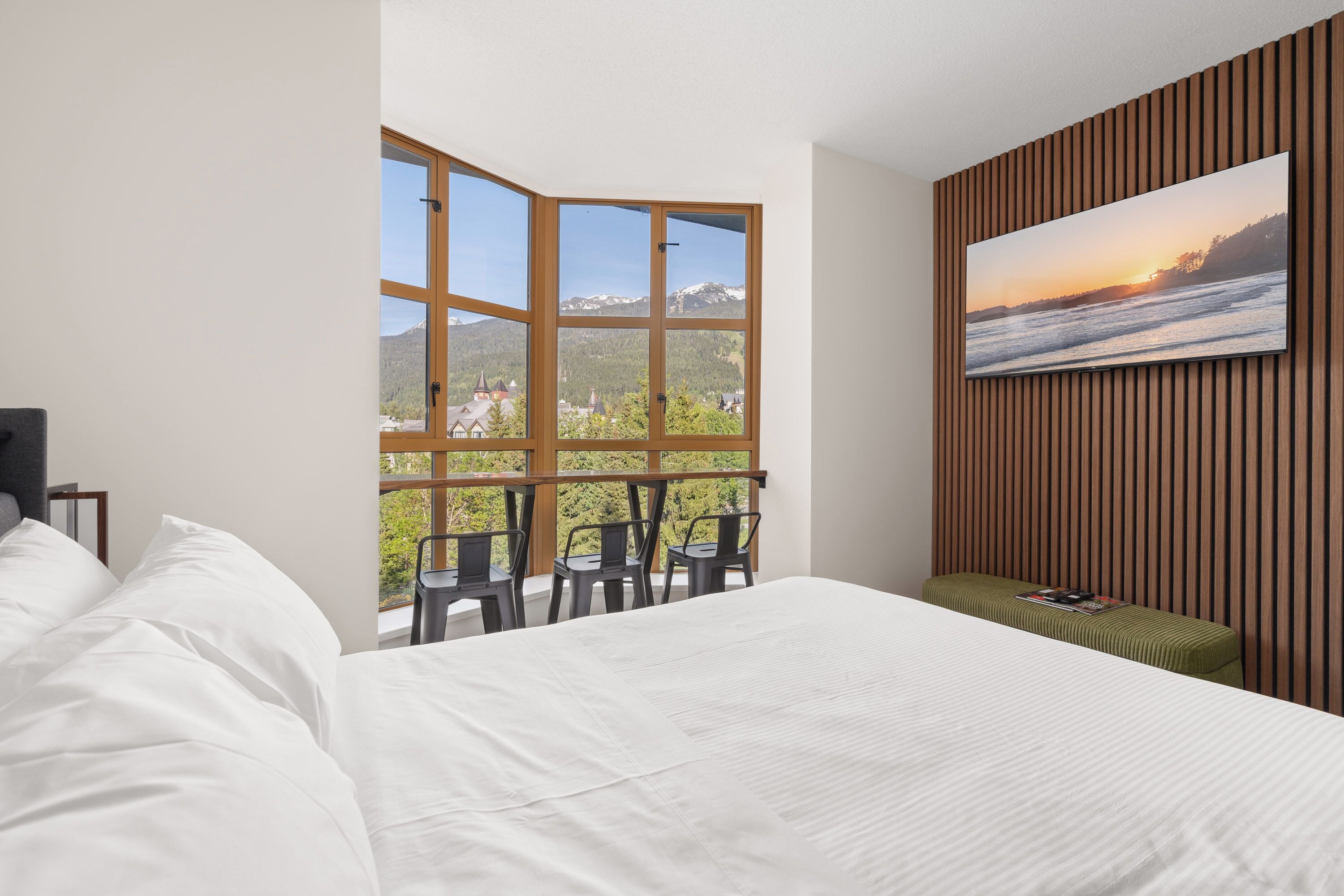 A hotel room with a large window, a bed, a seating area with chairs, and a television on the wall.