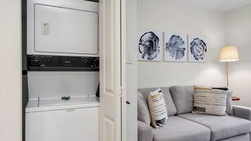 A laundry room with stacked appliances and a grey sofa with patterned cushions.