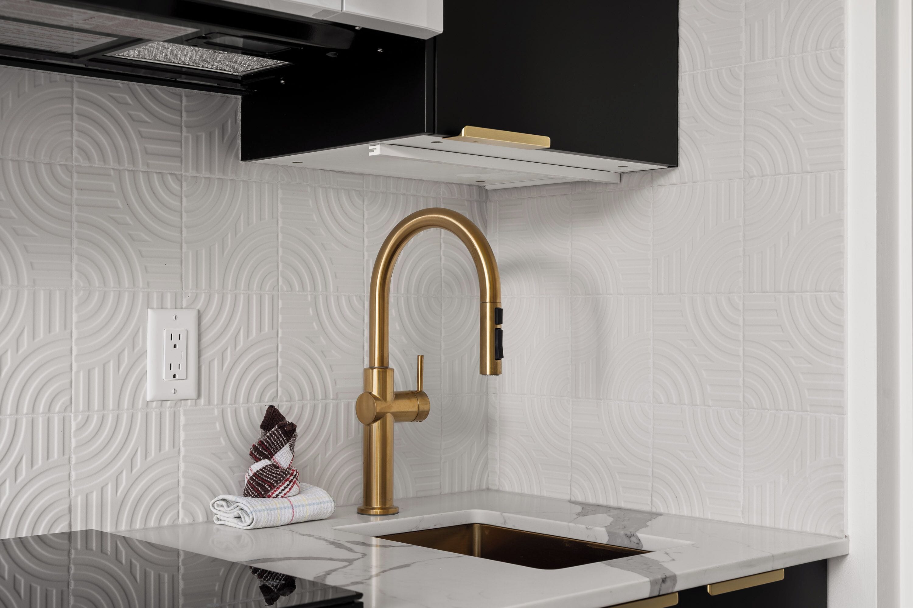 Una cocina moderna con grifo dorado, azulejos blancos y encimera de mármol.