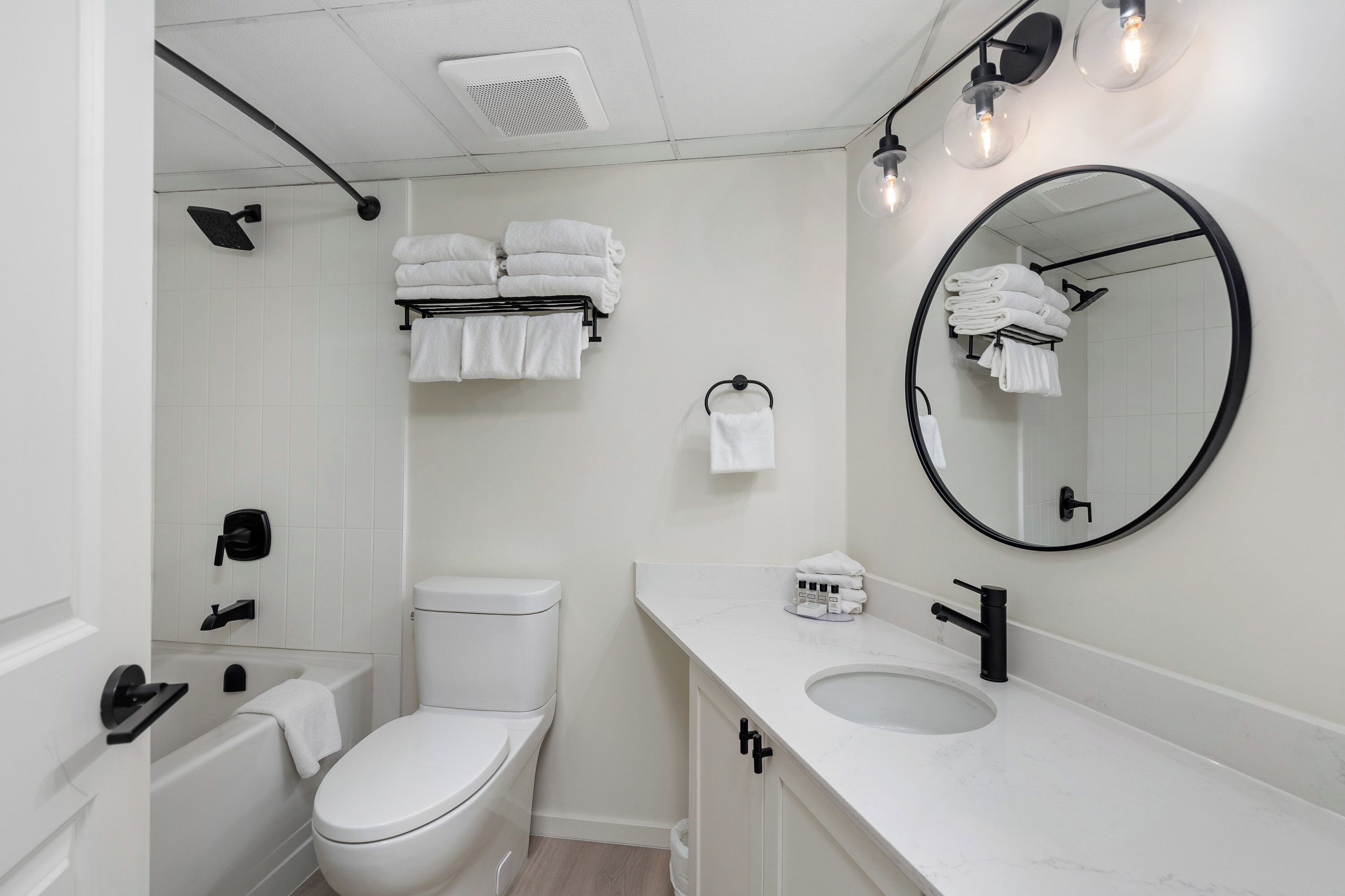 A modern bathroom with a white toilet, a bathtub, a sink, and a large mirror.