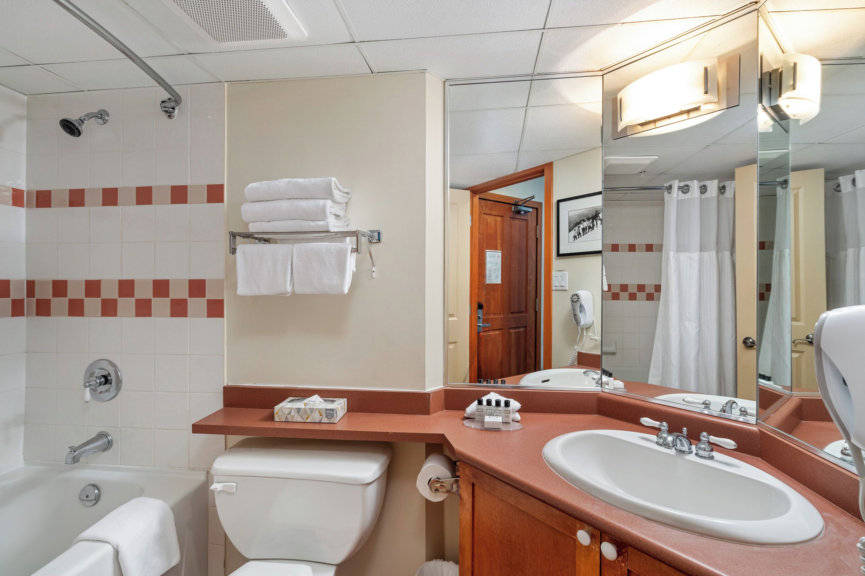 Et badeværelse med badekar, toilet, håndvask og et stort spejl.