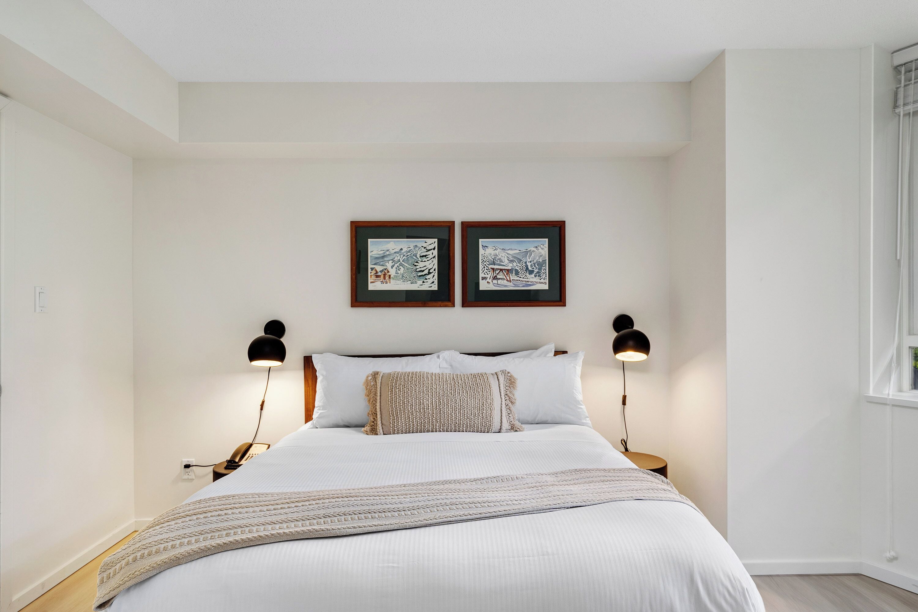 Ein ordentlich eingerichtetes Schlafzimmer mit einem großen Bett, zwei Wandleuchten und zwei Bildern im Bilderrahmen darüber.
