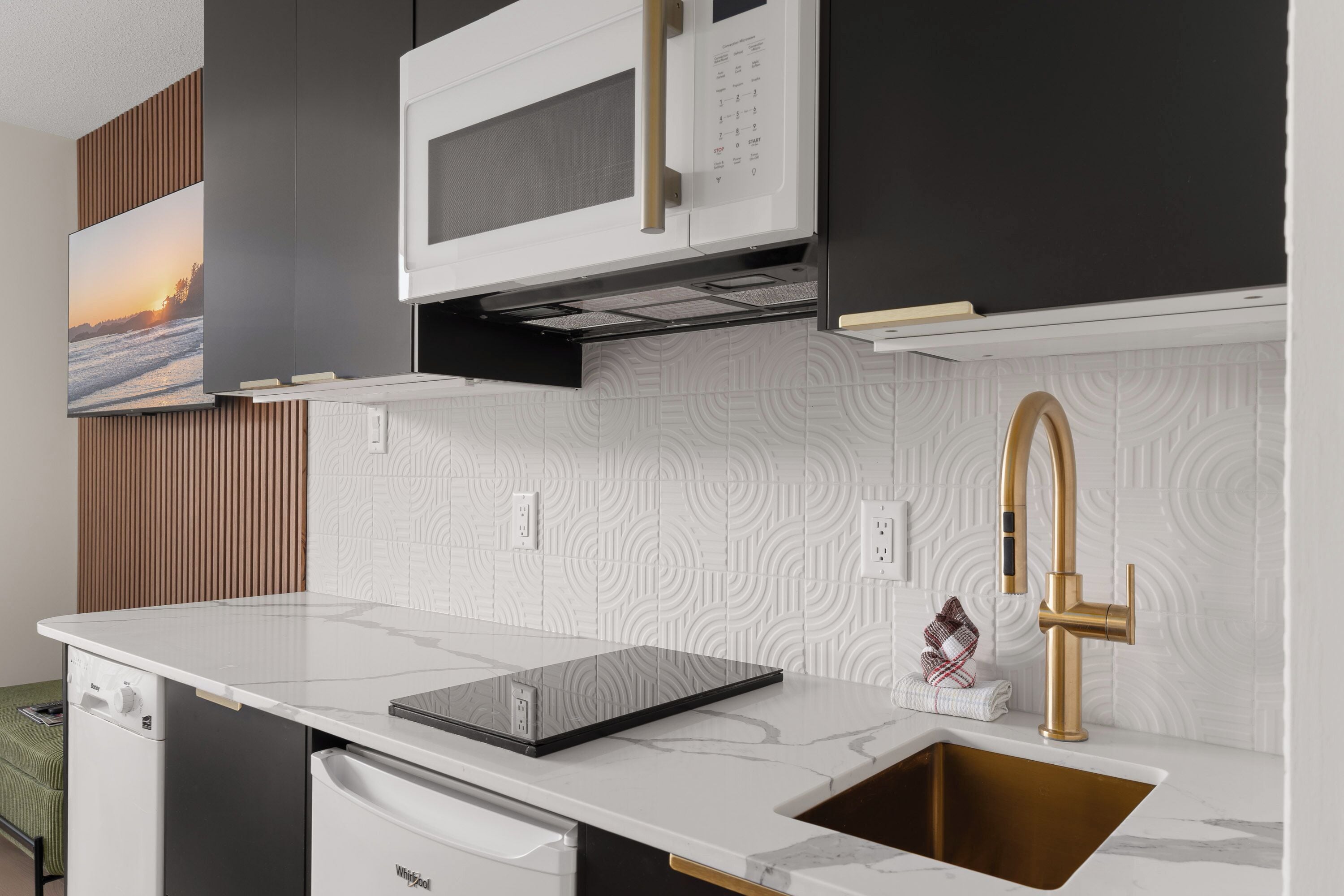A modern kitchen with a built-in microwave, a stainless steel sink with a gold faucet, and a patterned backsplash.
