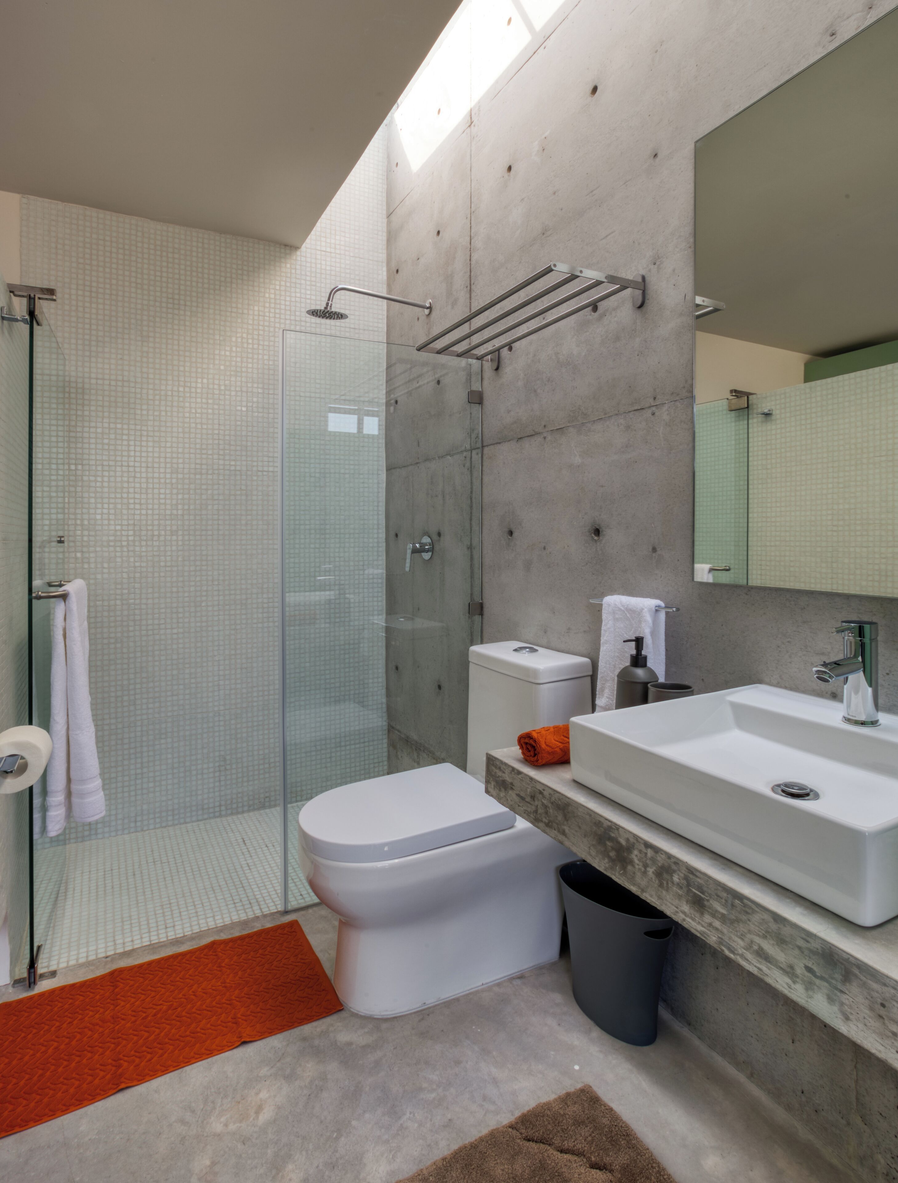 A modern bathroom with a glass shower enclosure, a white toilet, a large sink with a mirror, and a towel rack.