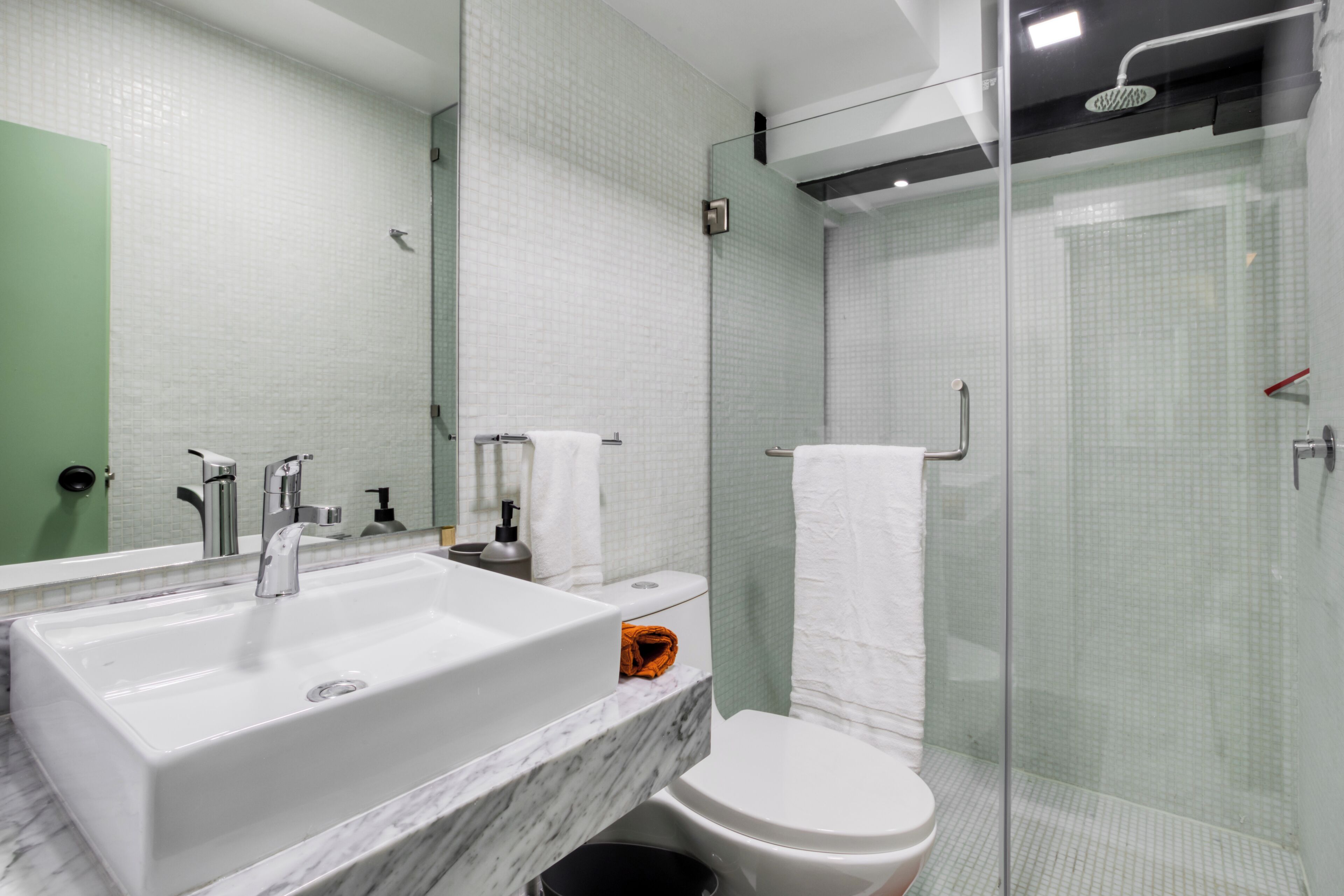 A modern bathroom with a large white sink, a toilet, and a glass-enclosed shower.