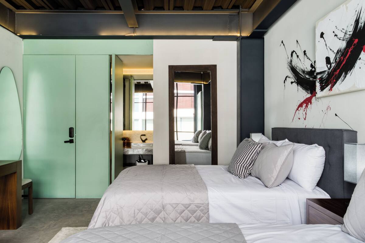 A modern bedroom with a large bed, a bedside table, a nightstand, a mirror, and a door leading to a bathroom.
