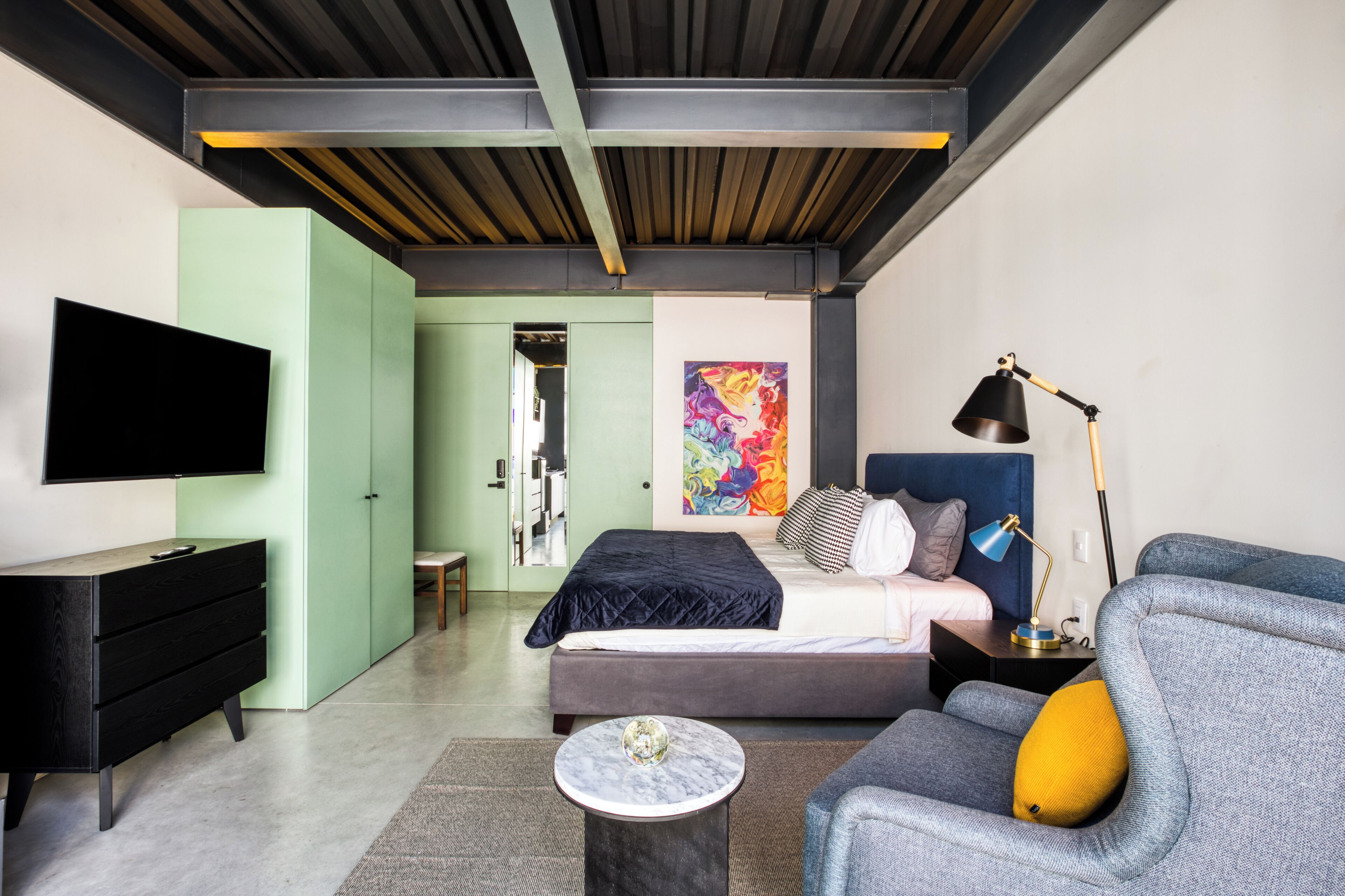 Une chambre à coucher moderne avec un lit, un bureau, une chaise, un téléviseur et un tableau au mur.