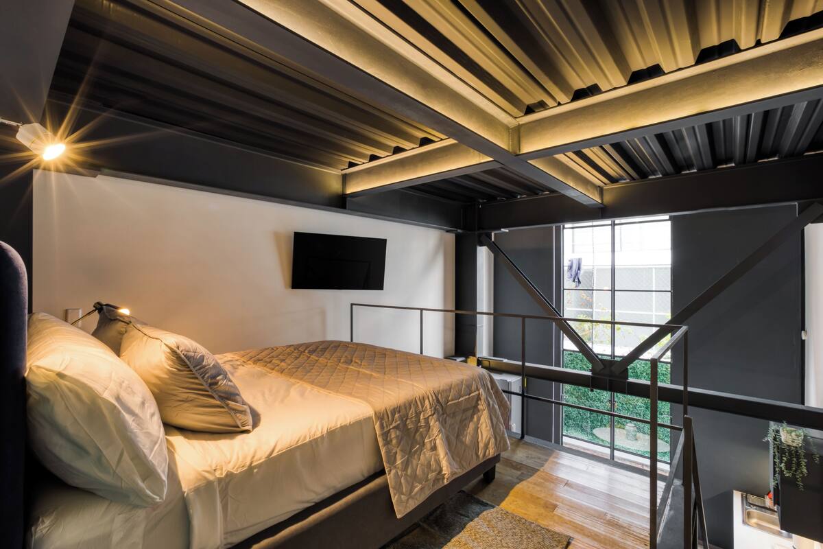 A modern bedroom with a bed, a TV, and a view of the outdoors.