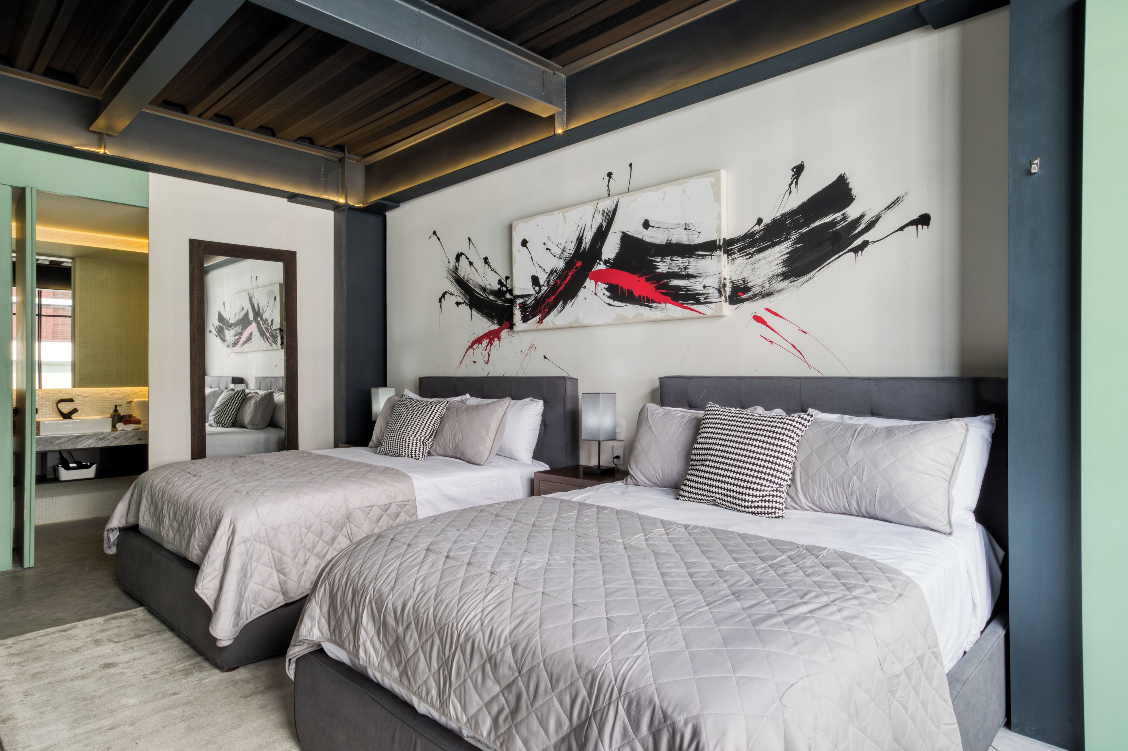 Ein modernes Hotelzimmer mit zwei Betten, einem großen abstrakten Gemälde an der Wand und einem durchgegangene Tür erkennbaren Badezimmer.