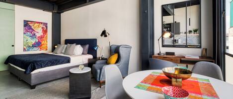 Un dormitorio moderno con cama, mesita de noche, silla y un comedor con mesa y sillas.