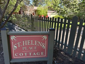 Placa indicando St. Helens Place Cottage, com uma cerca de madeira ao fundo.