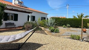 Une maison avec un toit en tuiles, un hamac et un jardin où poussent différentes espèces de plantes.