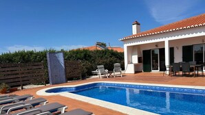 Une piscine avec des chaises longues, un patio couvert et un bâtiment doté d’un toit en tuiles.
