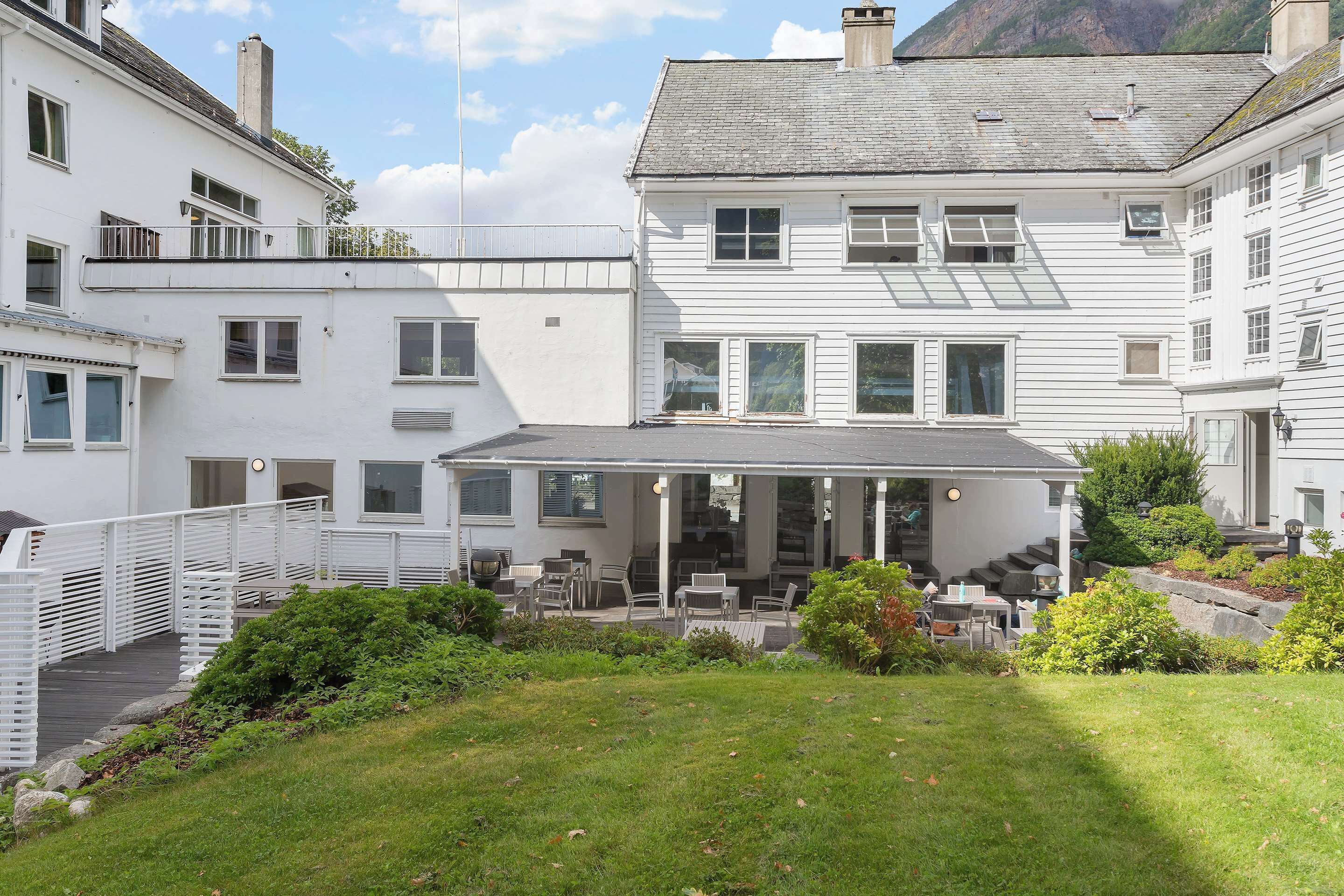 Ein weißes, zweistöckiges Gebäude mit überdachter Veranda und Gartenmöbeln.