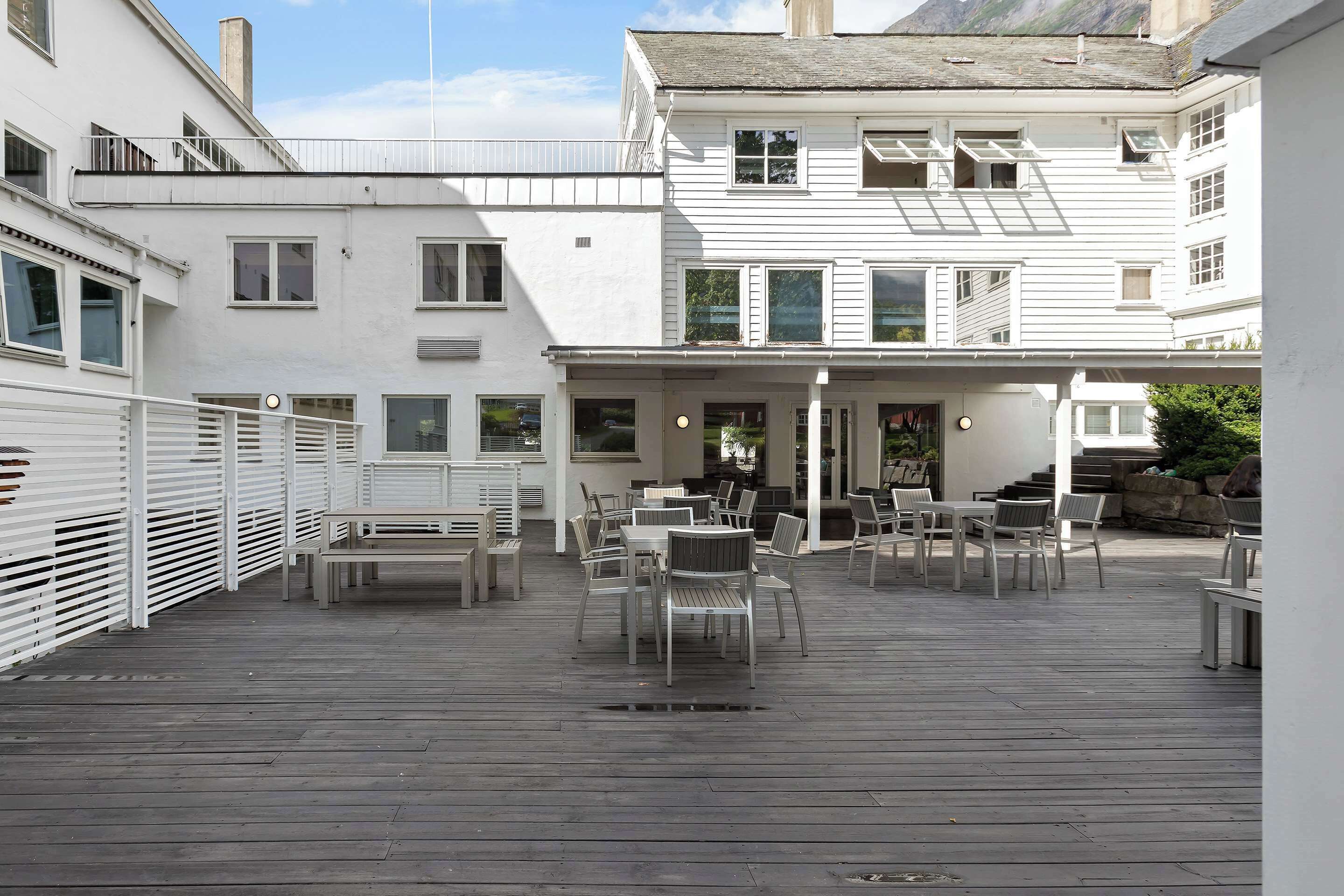 Un patio techado al aire libre con varias mesas y sillas, rodeado de edificios blancos con balcones.