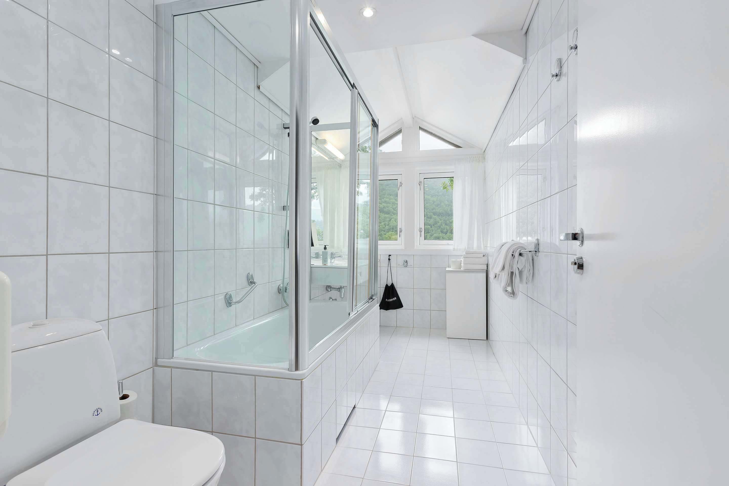 A modern bathroom with a glass-enclosed shower, white tiles, and a visible toilet.