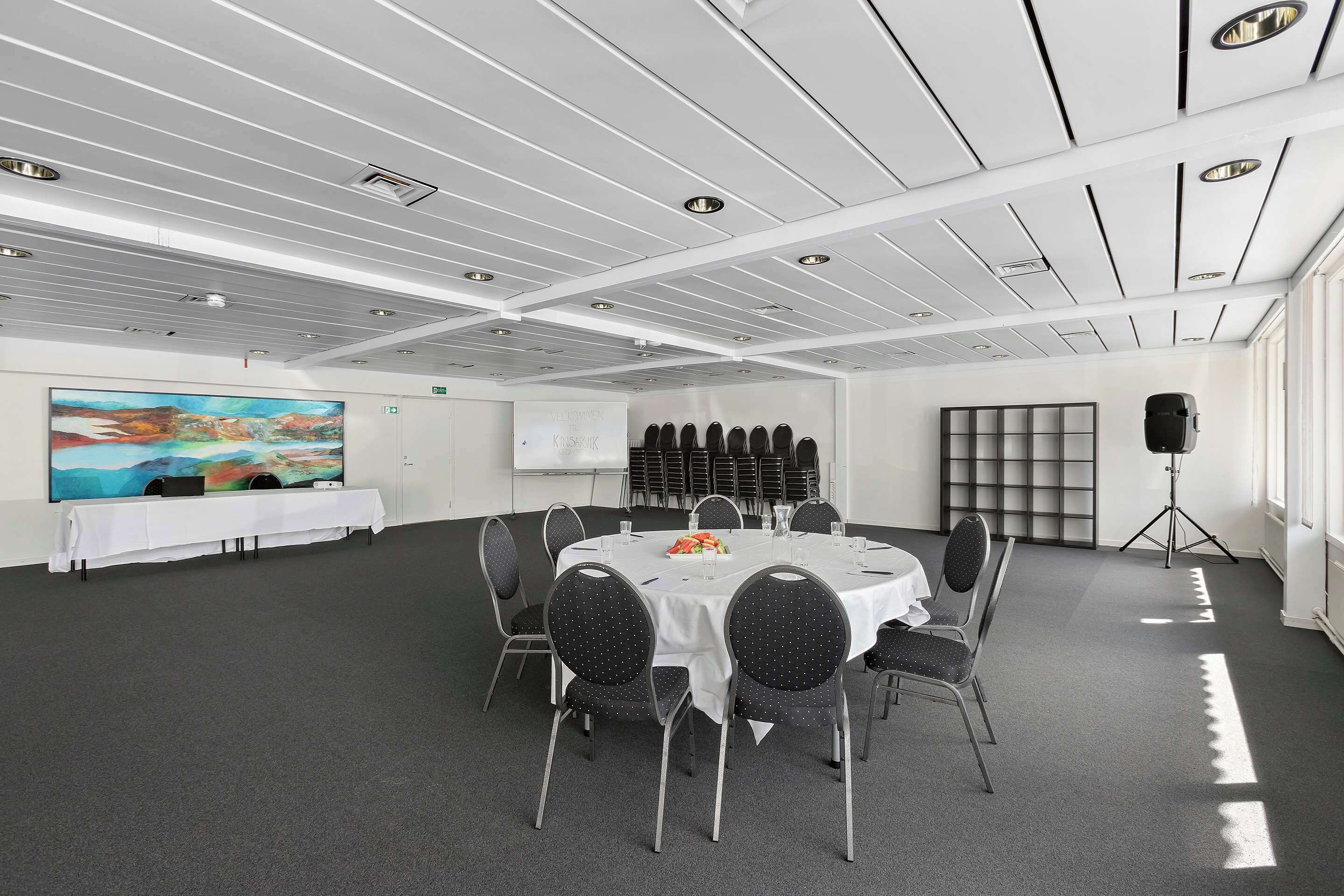 Un salón de conferencias con techo blanco, un cuadro grande, una pizarra y un soporte para proyector.
