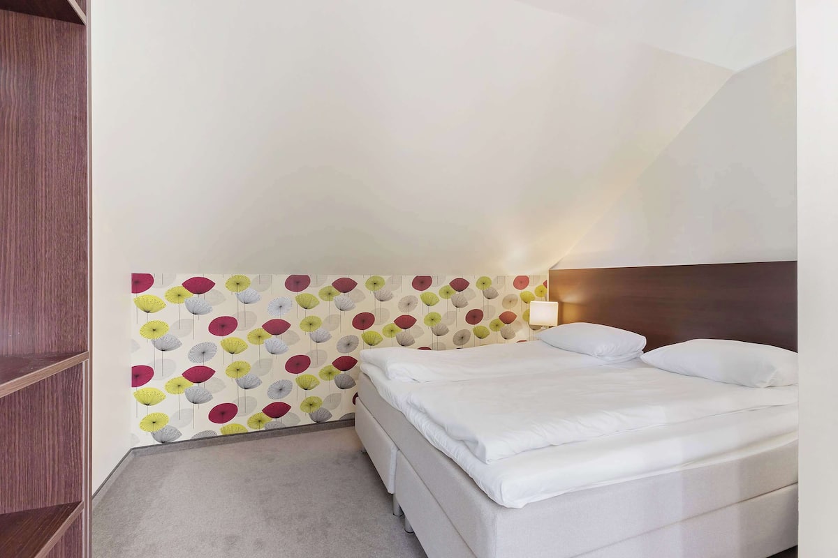 Habitació d'hotel amb un llit, una prestatgeria de fusta i una paret amb un dibuix colorit.