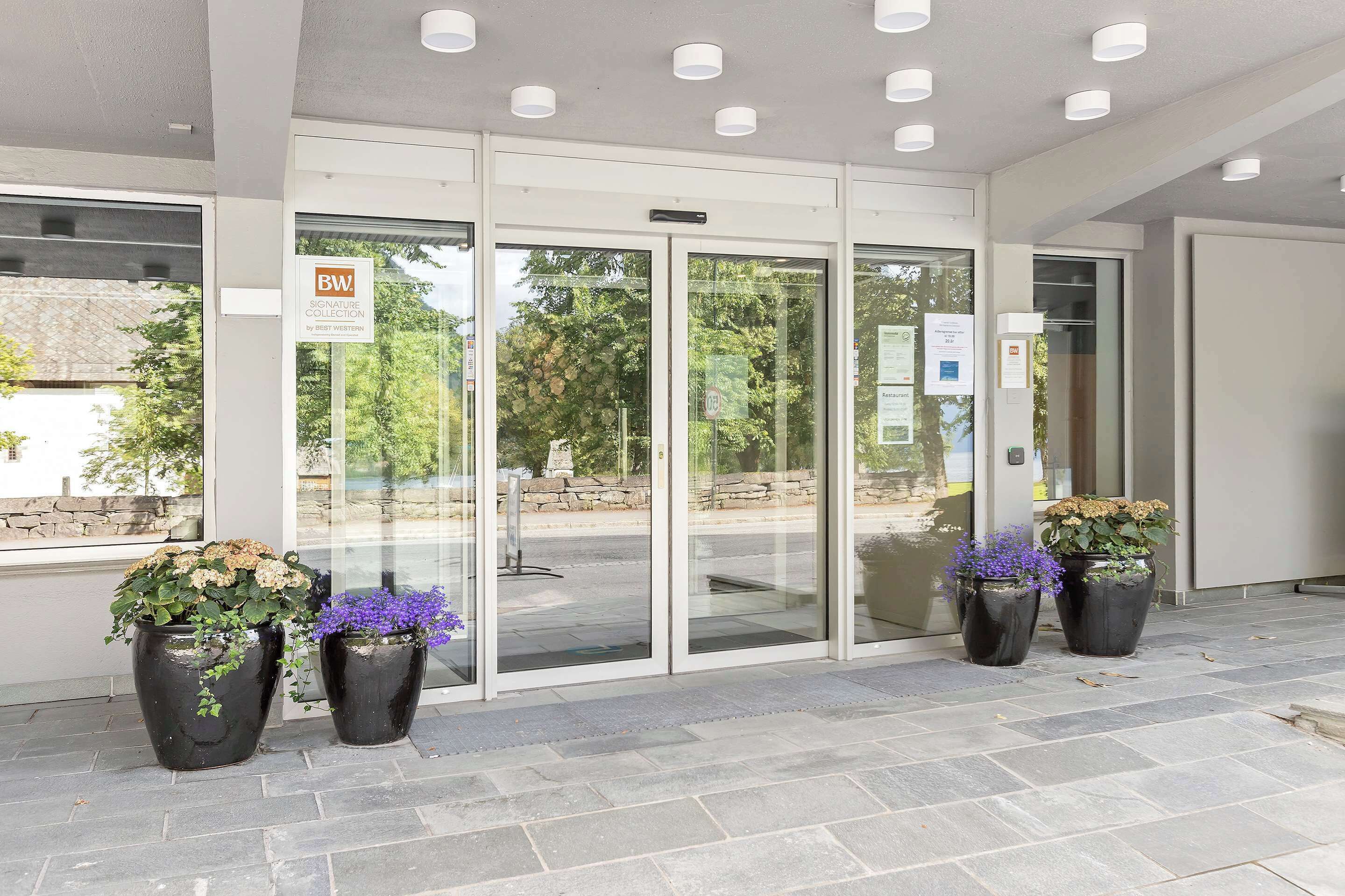 A modern building entrance with glass doors, potted plants, and a clear view of the outside.