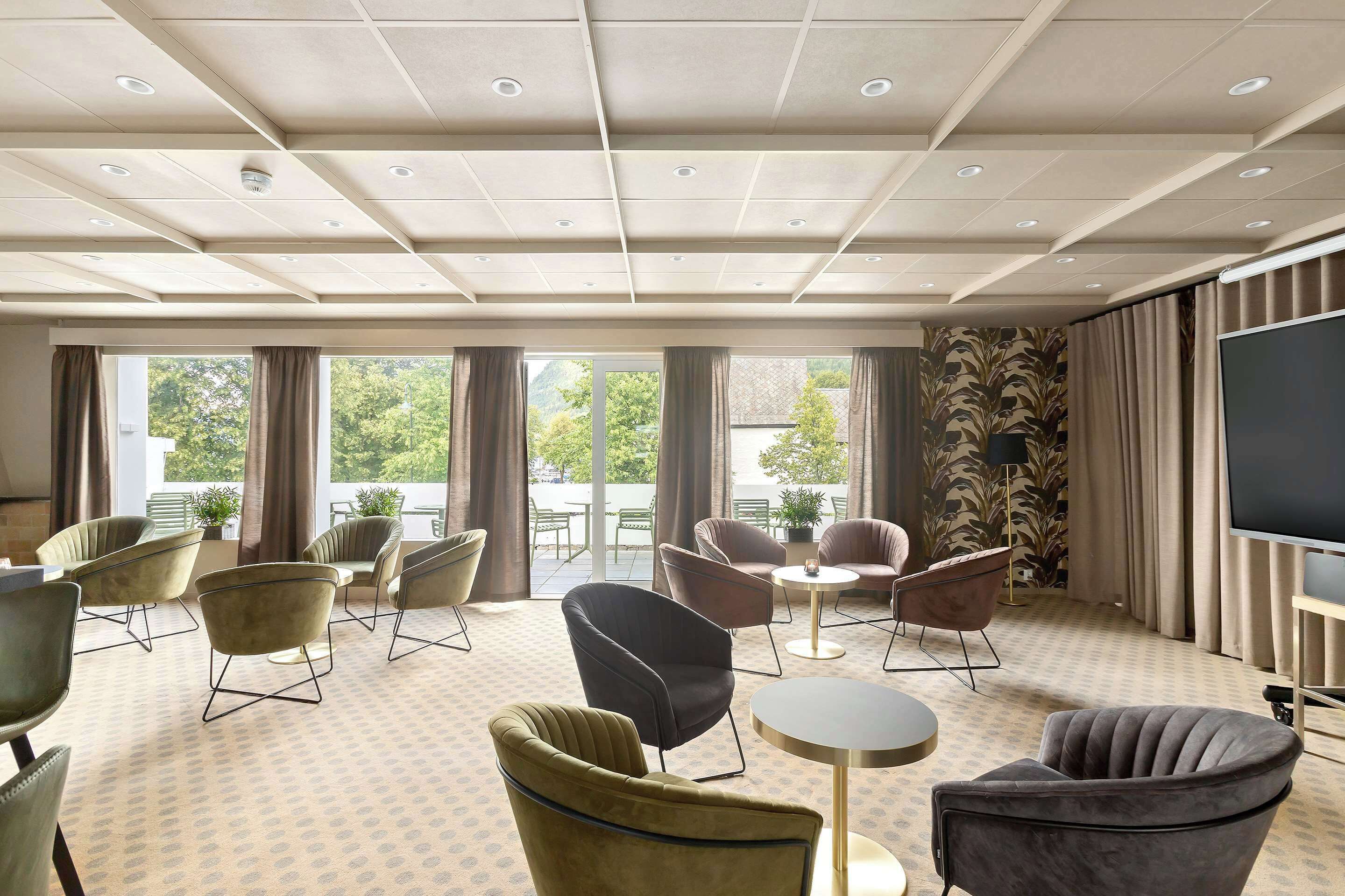 A hotel room with a large window, multiple seating areas, and a flat-screen TV.