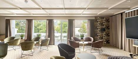 A hotel room with a large window, multiple seating areas, and a flat-screen TV.