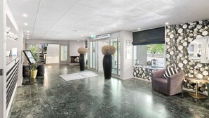 Eine moderne Lobby mit Marmorboden, einer Rezeption, einer Sitzecke mit einer Couch und großen dekorativen Vasen.
