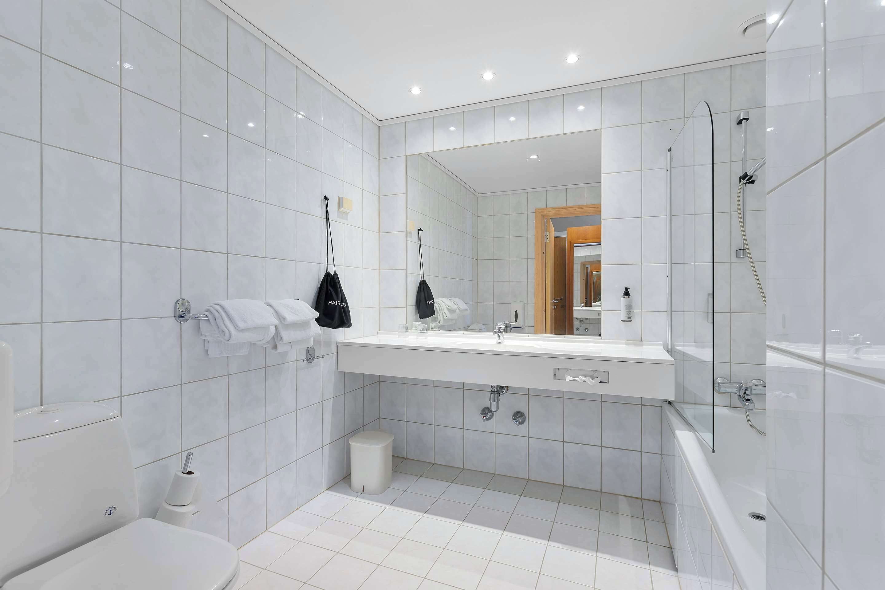 Une salle de bain moderne avec des carreaux blancs, un grand miroir, un lavabo, des toilettes et une douche.