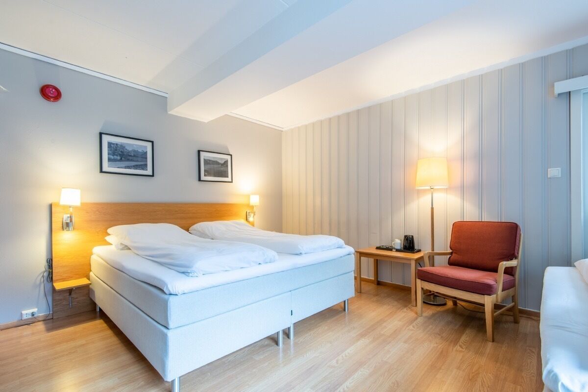 A hotel room with a bed, bedside tables, a chair, and a lamp.