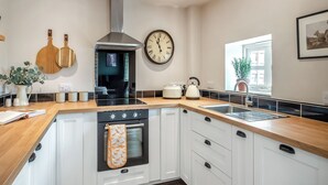 A modern kitchen with a built-in oven, a large clock, and wooden cutting boards on the wall. - The Hay Loft - UK45607 (Seaton, near Hornsea)