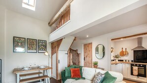 A spacious living area with a high ceiling, a dining table with chairs, a sofa with cushions, and a kitchen area with a stove and cabinets. - The Hay Loft - UK45607 (Seaton, near Hornsea)