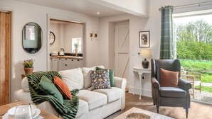 A cozy living room with a sofa, a chair, a table with dishes, and a view of the outdoors. - The Hay Loft - UK45607 (Seaton, near Hornsea)