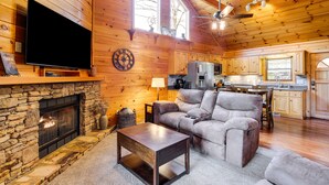 Een gezellig interieur van een chalet met een stenen openhaard, een flatscreen televisie, een comfortabele bank en een keukenhoek.