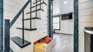 A modern interior with a wooden staircase, a drawer with various items, and a window providing natural light. - Broken Bow Cabin w/ Hot Tub, Fire Pit & Creek View (Broken Bow)