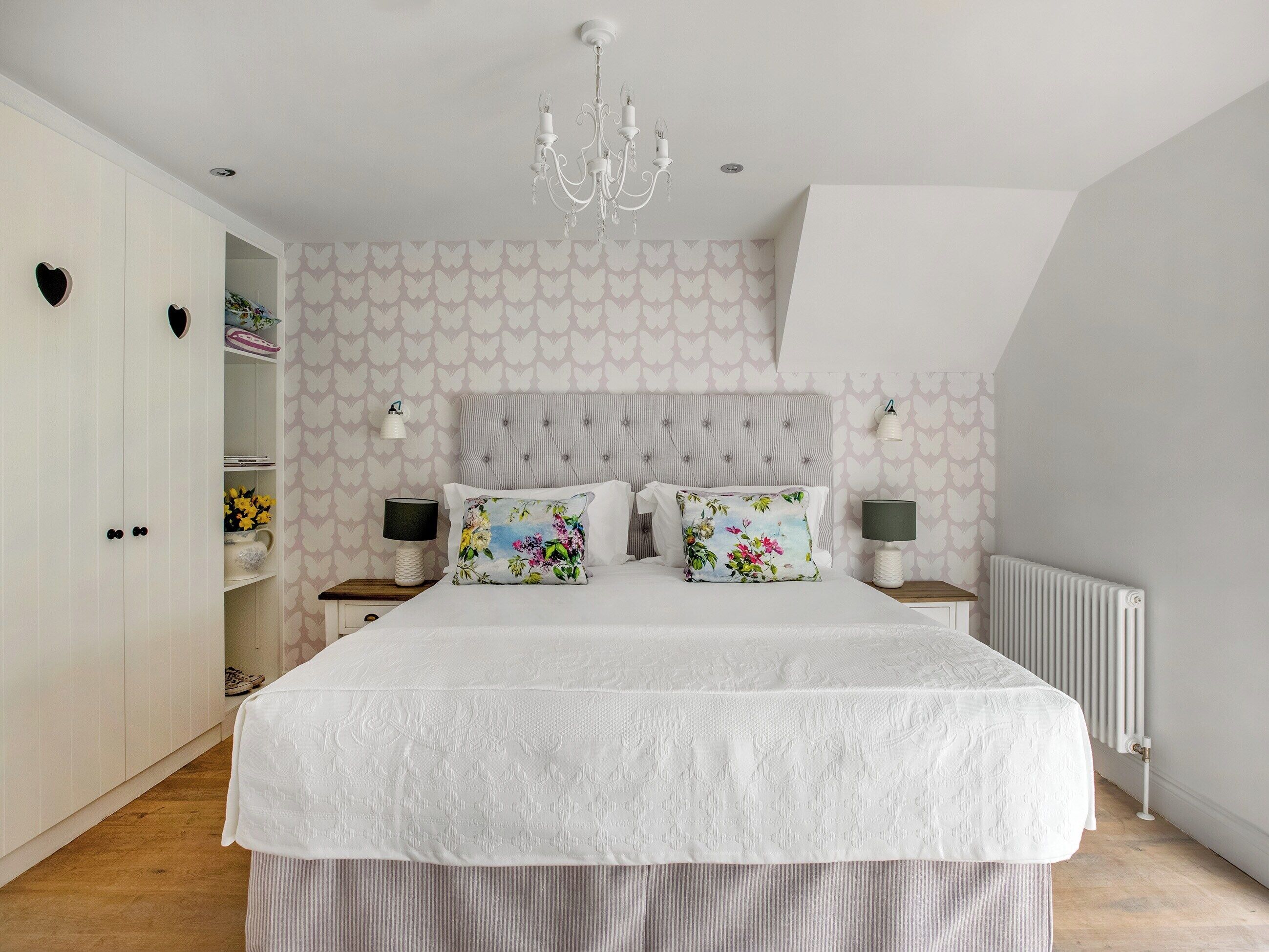 A bedroom with a large bed, a chandelier, a wardrobe, and a radiator.