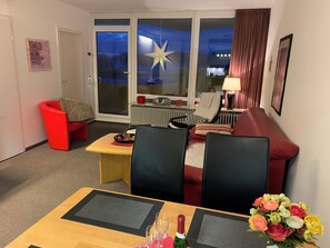 Una sala de estar con un sofá rojo, una mesa de comedor con sillas, un radiador y una ventana decorada con una estrella.
